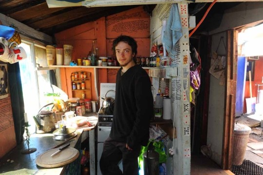 Angus Chalmers, a 20-year-old from Edinburgh and two year veteran of the camp, in the communal kitchen. A myriad of simple, hearty recipes are scrawled on the room's walls.